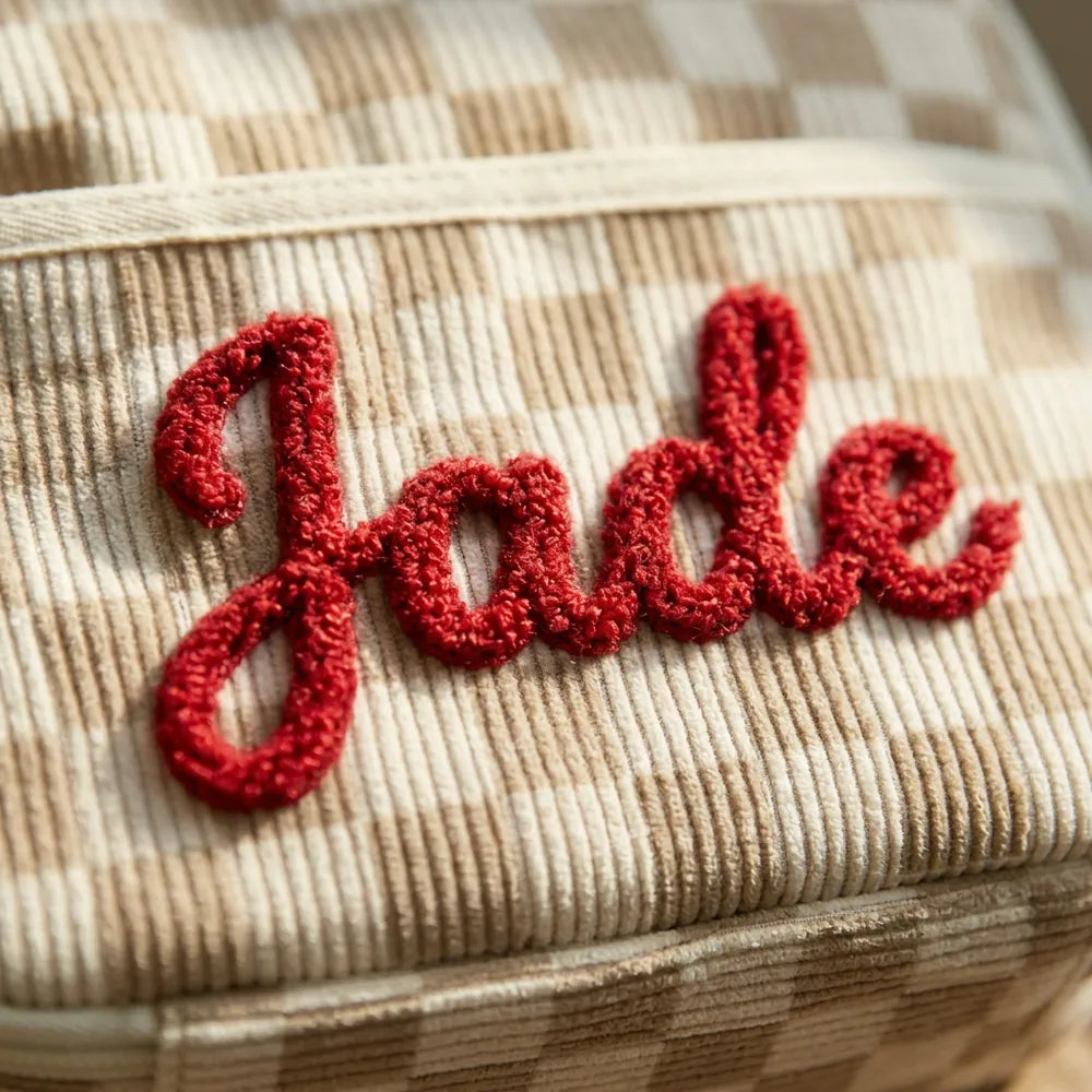 Gros plan de la broderie en laine bouclée rouge du prénom Jade sur le velours à damier