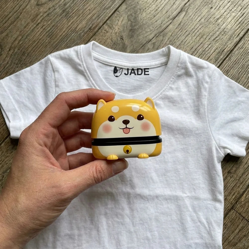 Tampon prénom Shiba tenu dans une main d'adulte au-dessus d'un t-shirt enfant marqué Jade